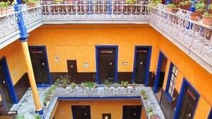 A courtyard with a central open area, surrounded by buildings with blue doors and orange walls. - Hotel Isabel (Mexico City)