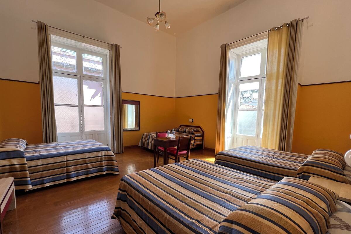 Habitación de hotel con dos camas, una mesita, una silla y una ventana con cortinas.
