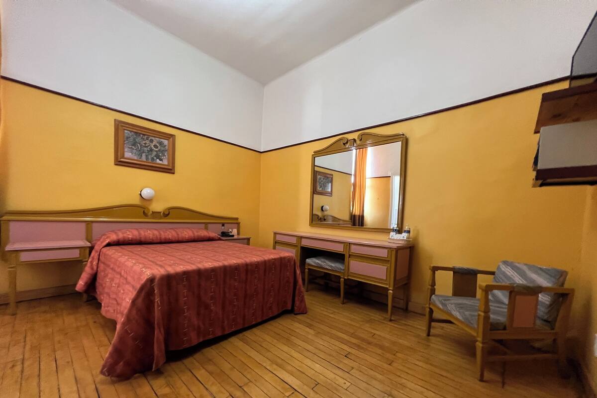 Un dormitorio con una cama de madera, una mesita de noche, un aparador, una silla y un espejo grande.