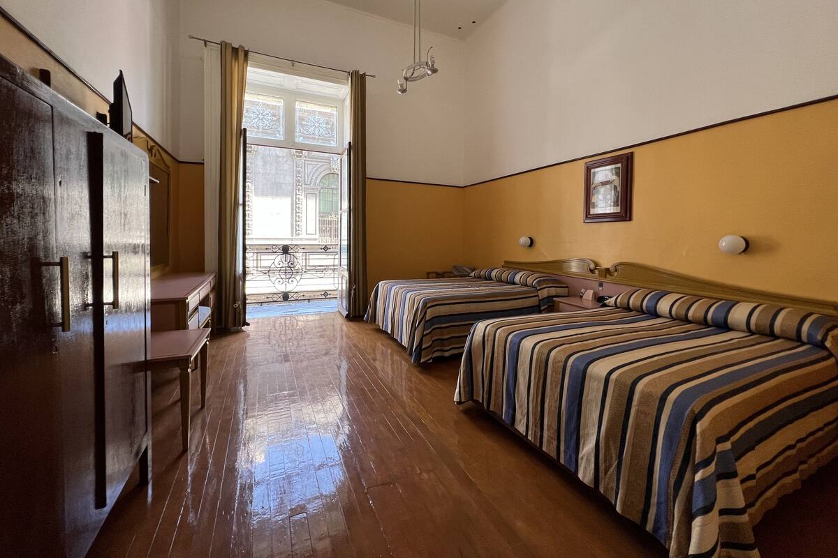 Habitación de hotel con dos camas, suelo de madera, un escritorio y una ventana con cortinas.