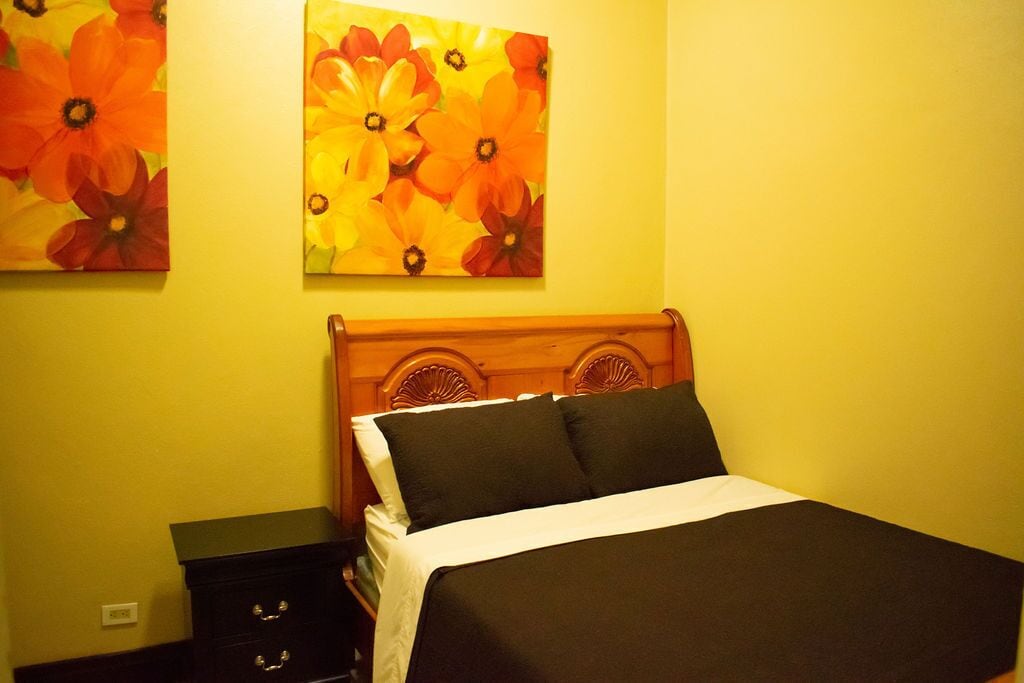 A room with a wooden bed, black bedding, and two floral paintings on the wall.