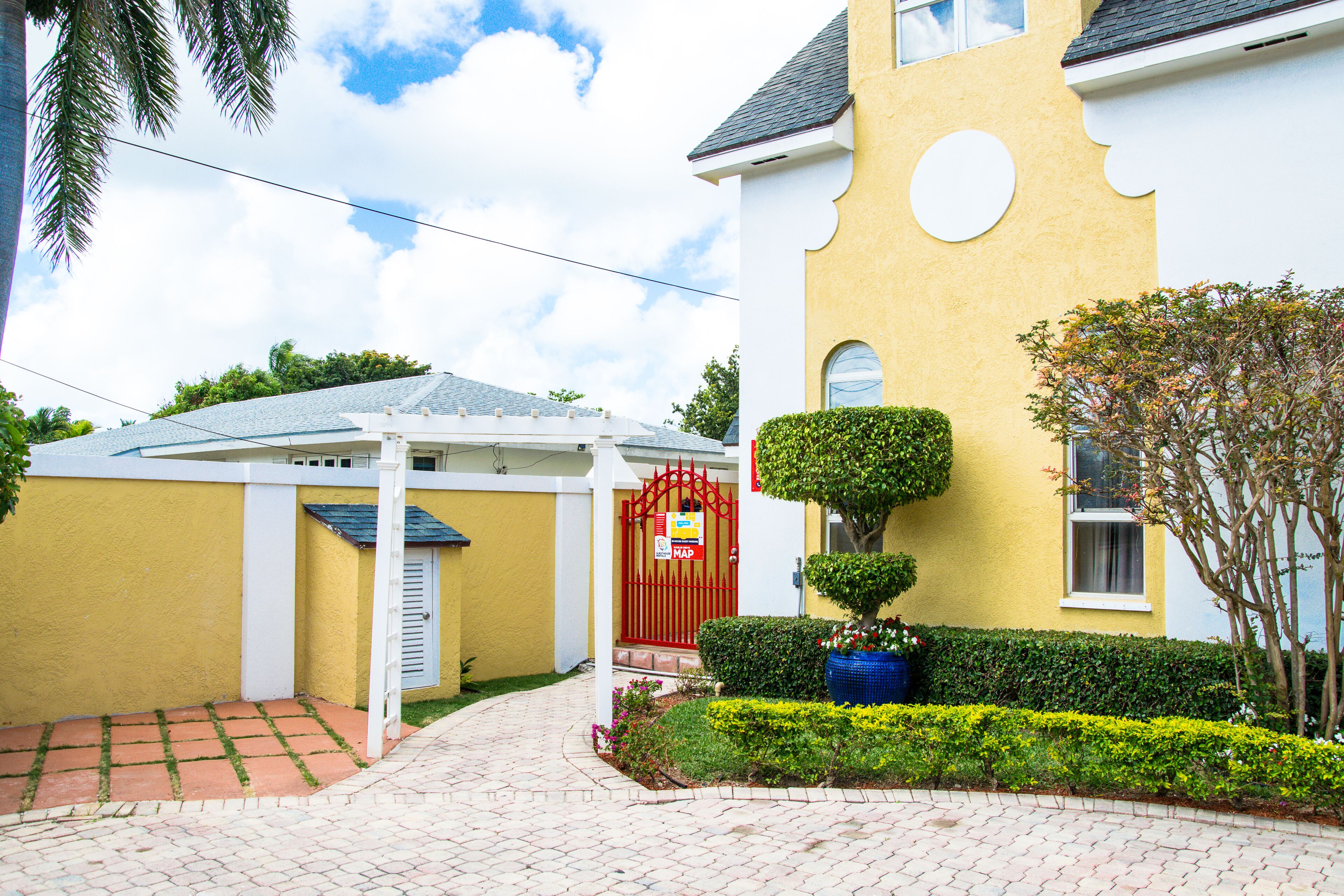 A yellow building with a red gate, a covered patio, and well-maintained landscaping.