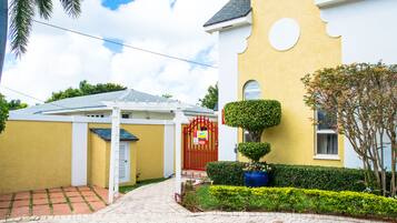 A yellow building with a red gate, a covered patio, and well-maintained landscaping.