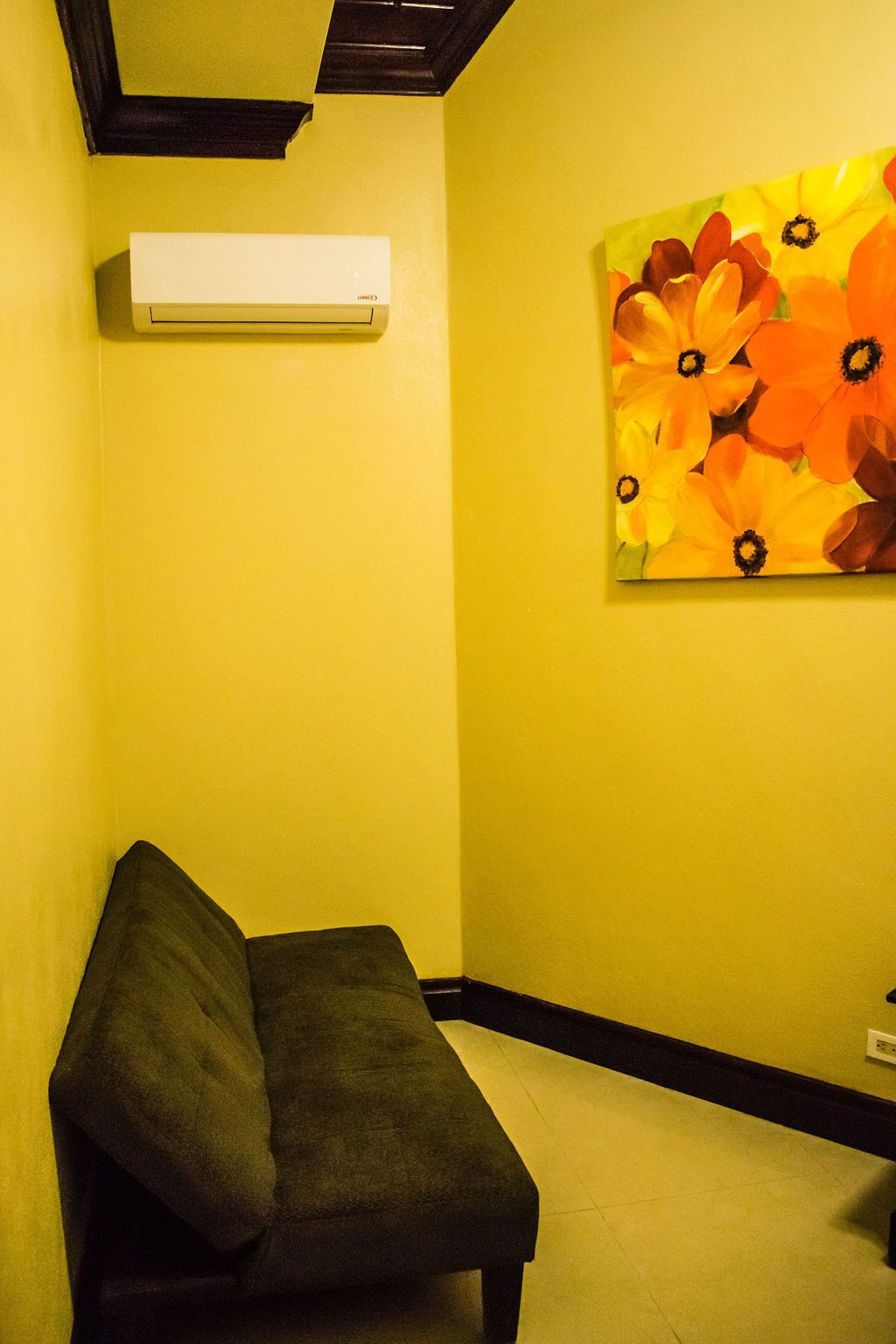 A room with a bench, an air conditioning unit, and a floral painting on the wall.