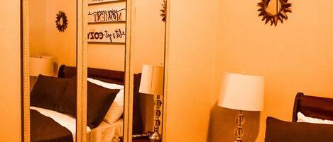 A hotel room with a large mirror, a bed, a nightstand with a lamp, and a wall decoration.