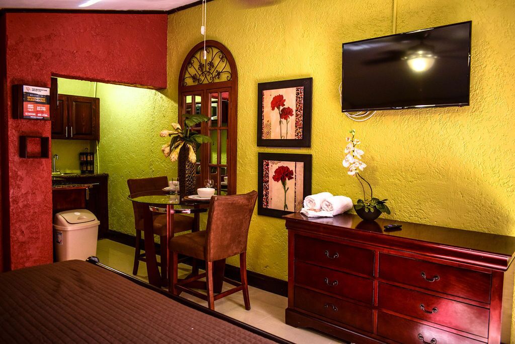 A hotel room with a dining area, a TV mounted on the wall, and a red cabinet.