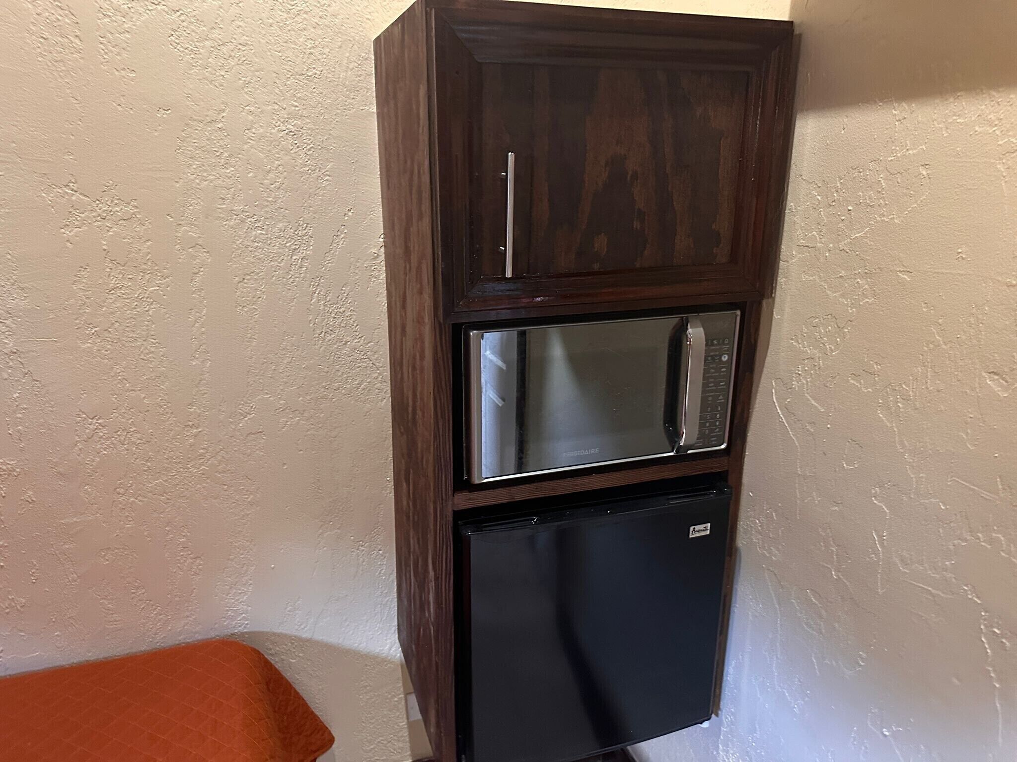 A built-in microwave and refrigerator unit with a wooden cabinet.