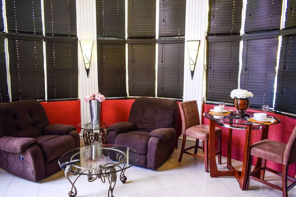 A modern living room with dark-colored sofas, a glass coffee table, and a dining area with a table set for two.