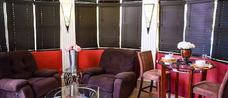 Una sala de estar moderna con sofás oscuros, una mesa de centro de vidrio y un comedor con una mesa preparada para dos.