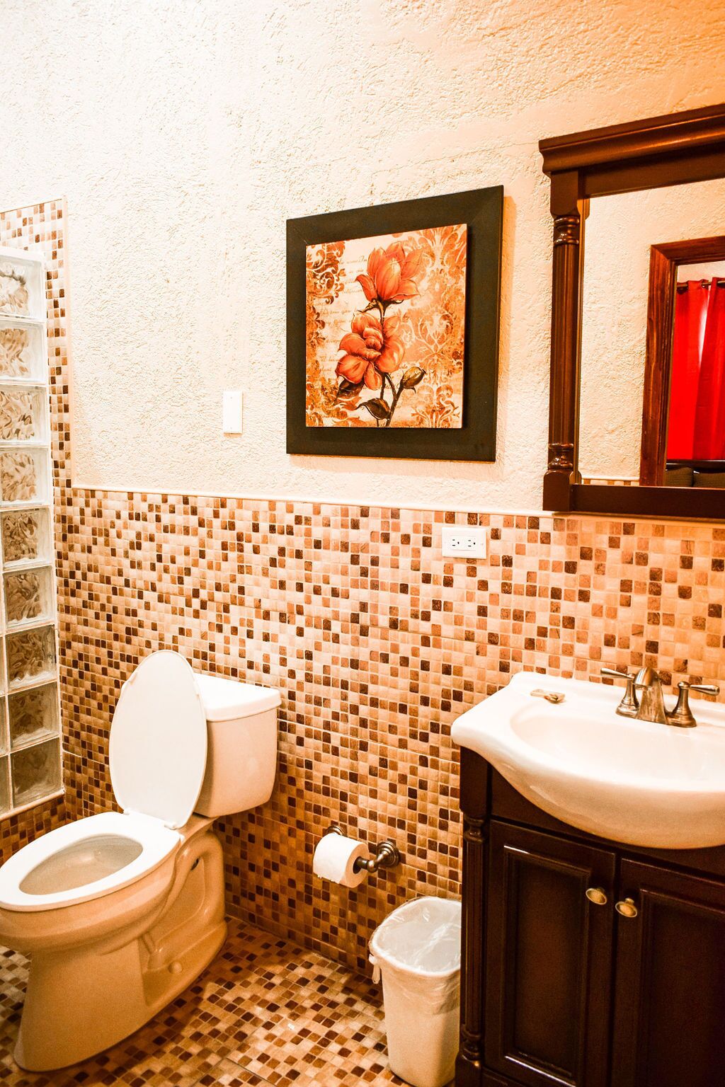 Un baño con inodoro, lavamanos y una obra de arte floral enmarcada en la pared.