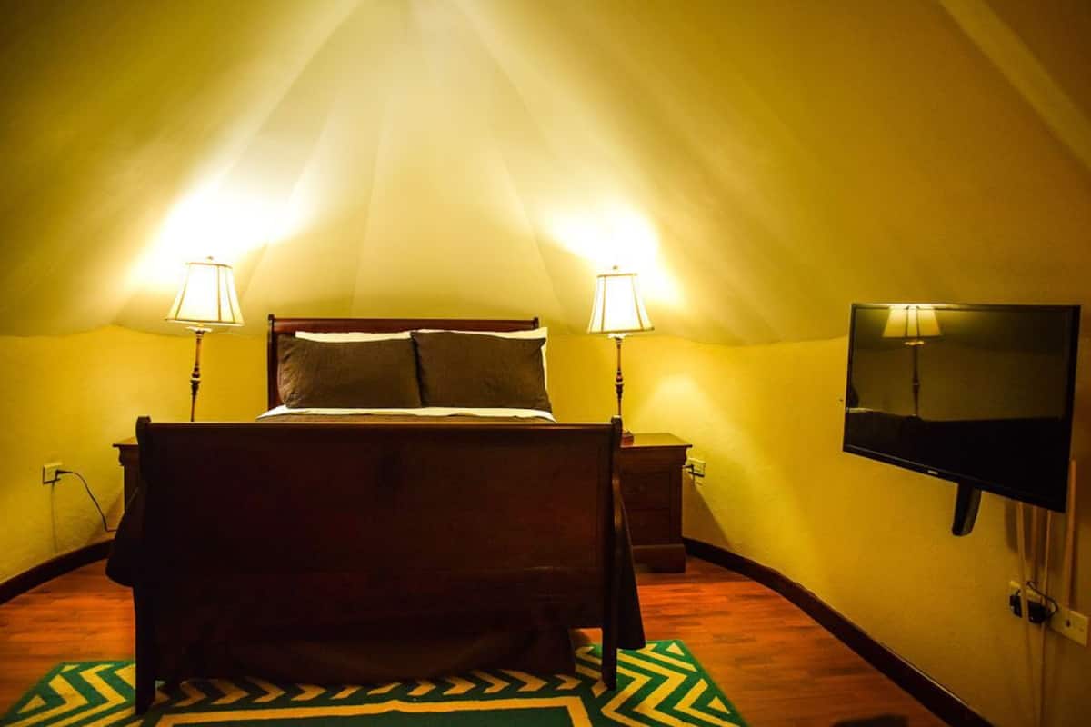 A bedroom with a bed, two bedside lamps, a television on the wall, and a patterned rug.