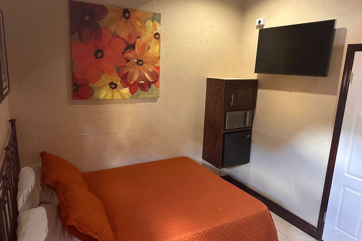 A bedroom with a bed, a painting, a wardrobe, and a TV mounted on the wall.
