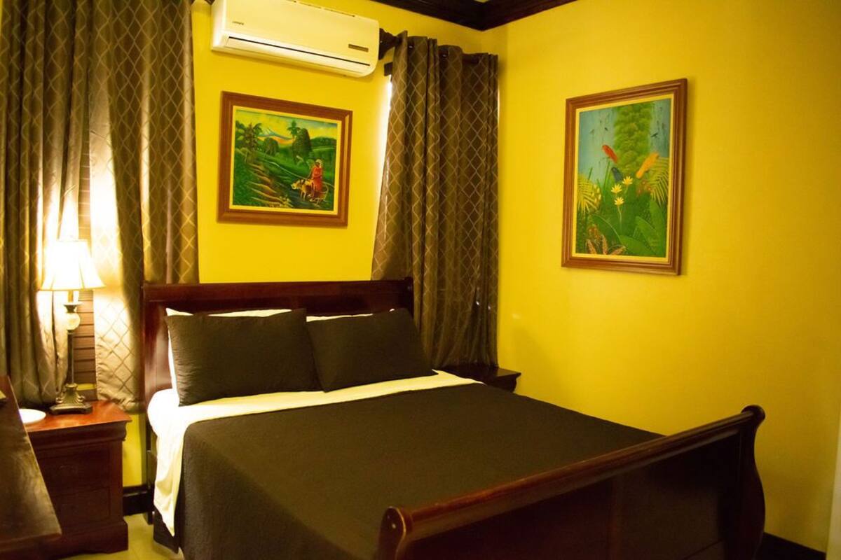 A hotel room with a bed, a nightstand, a lamp, and two framed paintings on the wall.