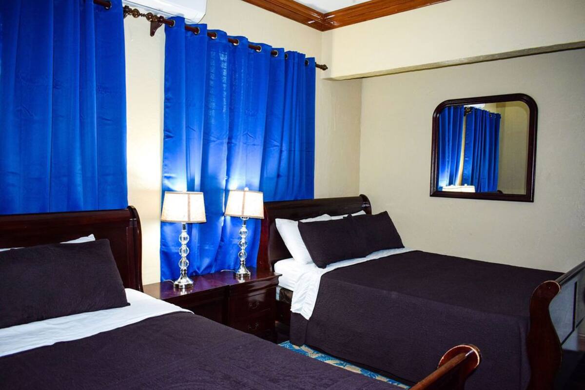 A hotel room with two beds, a large mirror, and blue curtains.