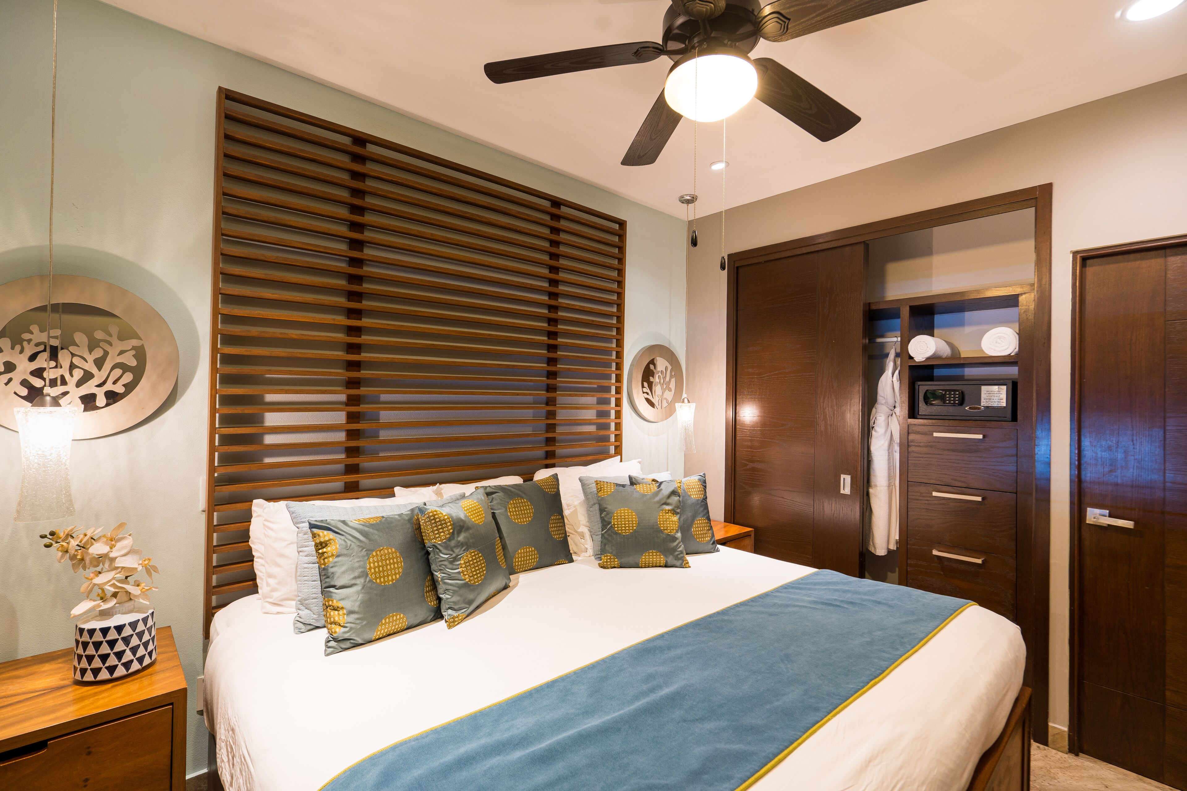 Une chambre à coucher avec un lit, des stores en bois, un ventilateur de plafond, une table de chevet et une armoire.