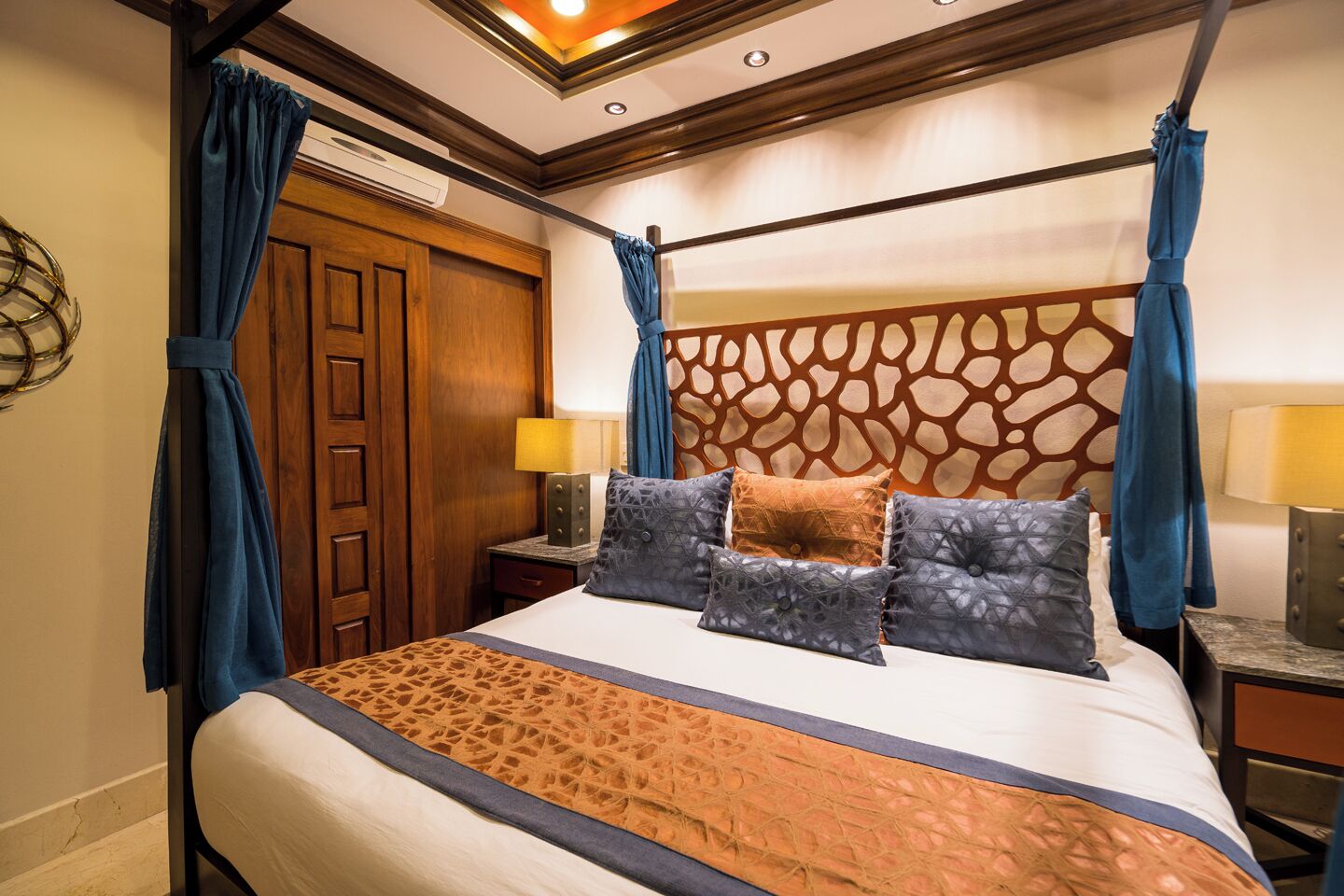 A four-poster bed with a patterned bedspread, multiple pillows, and a decorative headboard.