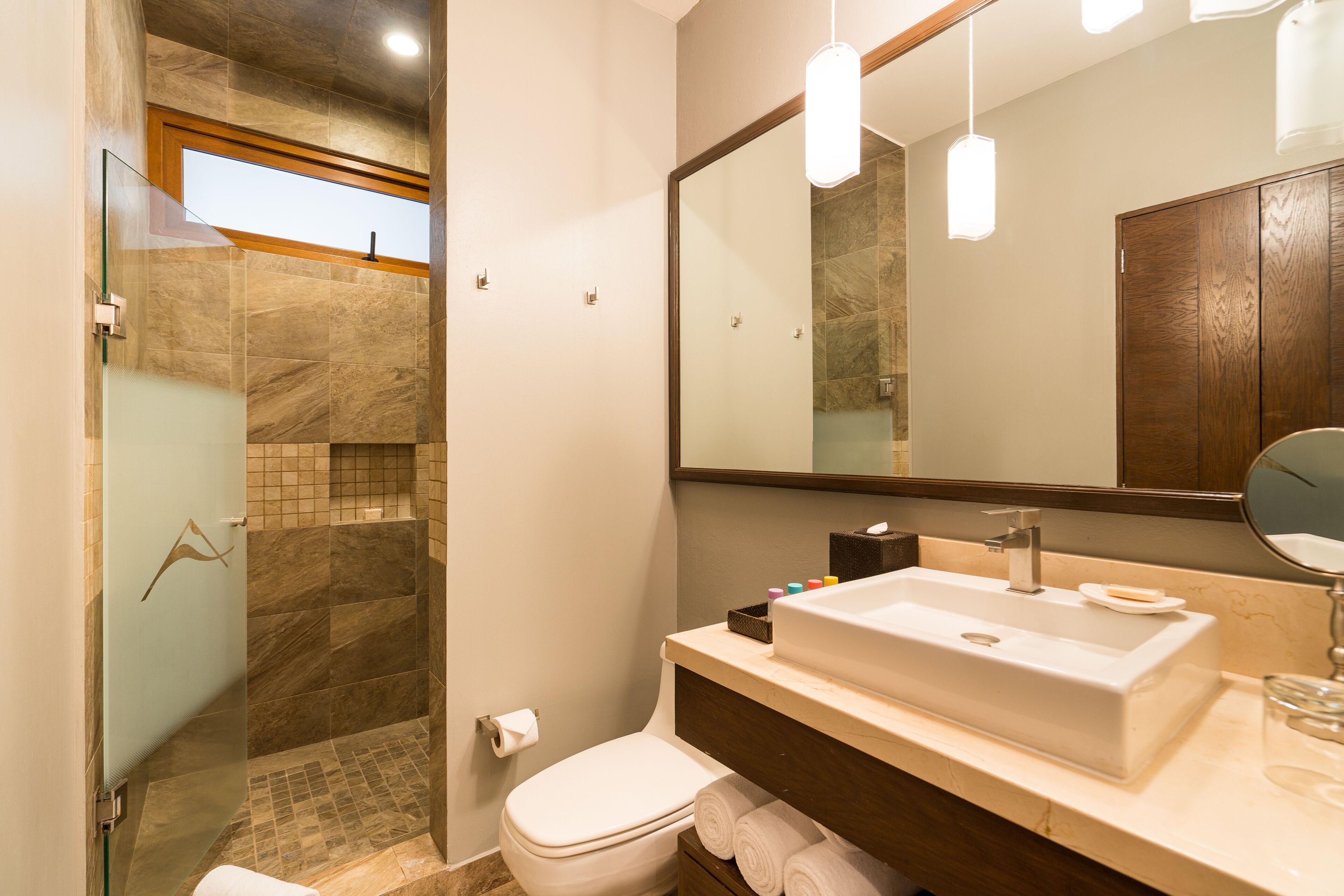 A modern bathroom with a glass shower enclosure, a white toilet, a large mirror, and a beige sink.