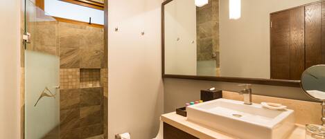 A modern bathroom with a glass shower enclosure, a white toilet, a large mirror, and a beige sink.
