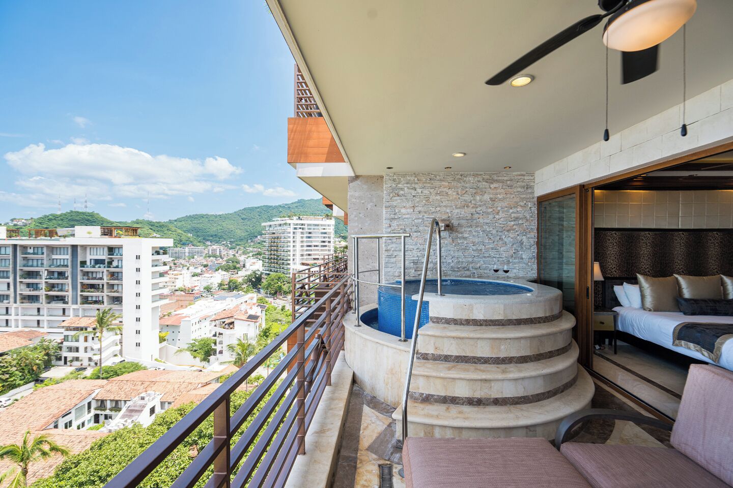 Un balcon avec un jacuzzi, un lit et une vue sur la ville.