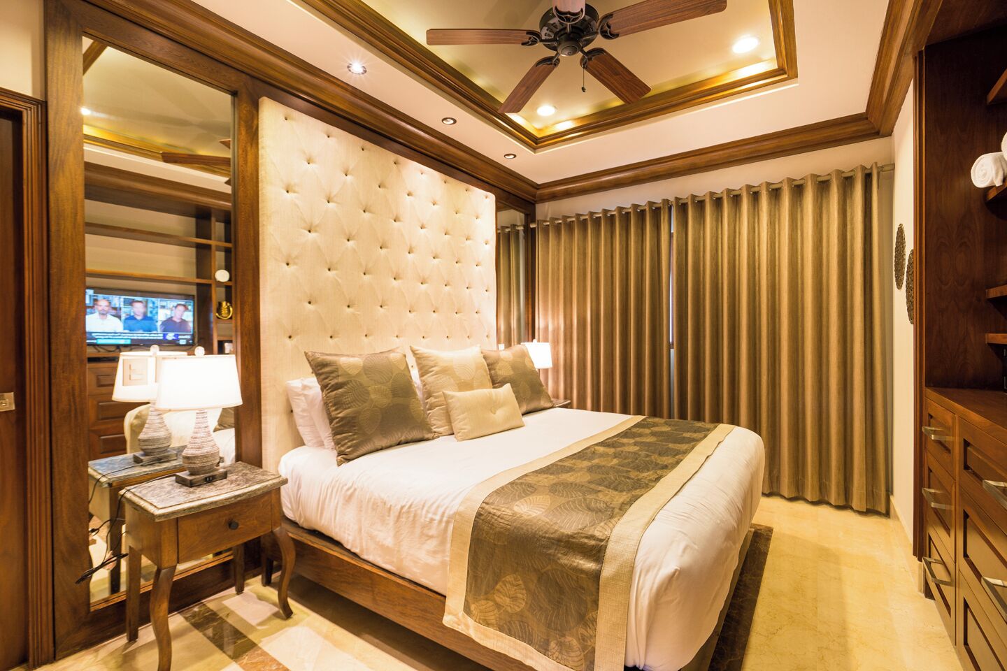 Une chambre spacieuse avec un grand lit, un ventilateur de plafond et un téléviseur posé sur un meuble.