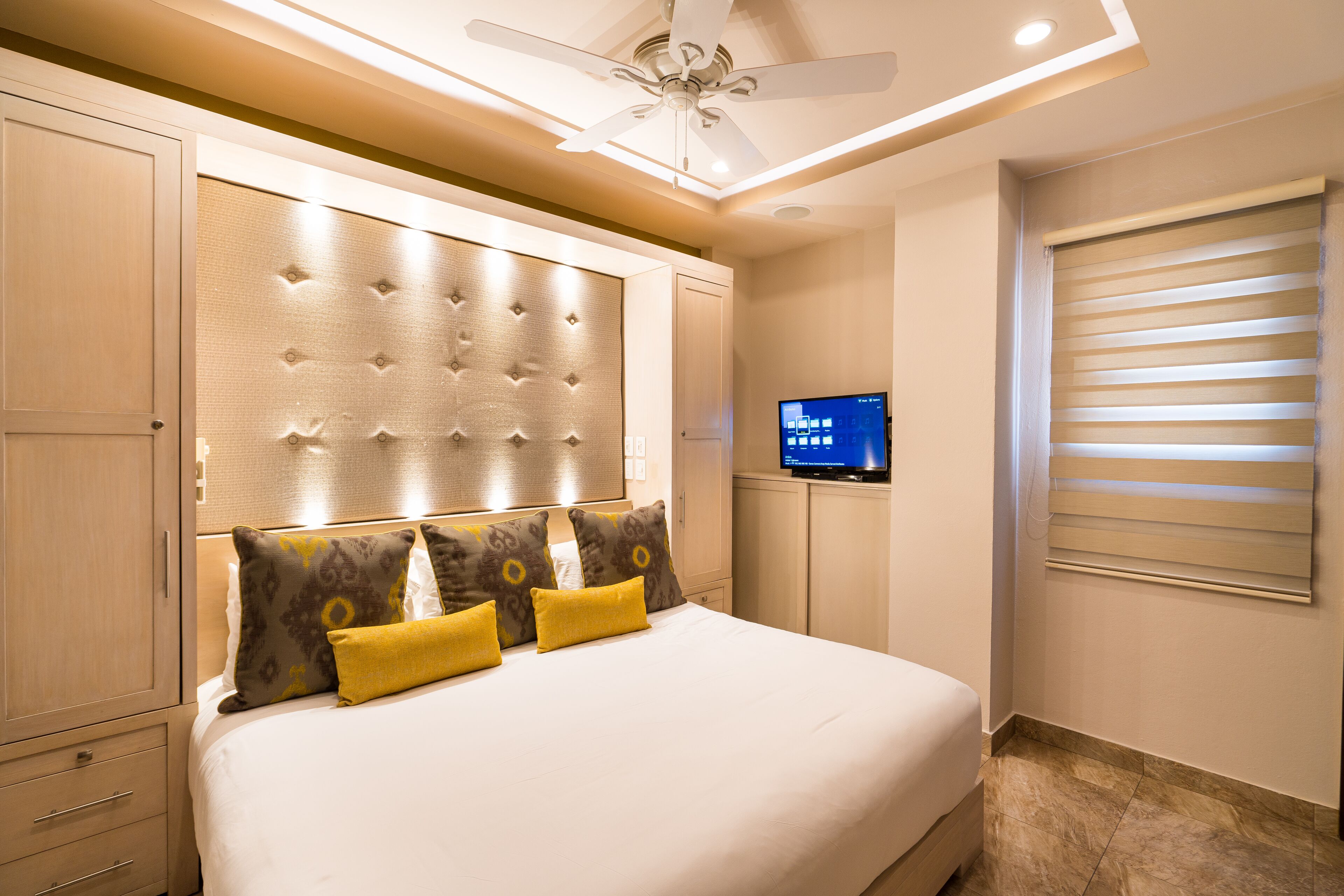 A hotel room with a large bed, a television, and a ceiling fan.