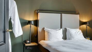 A neatly made bed with white linens, two bedside lamps, a wooden nightstand, and a robe hanging on a door.