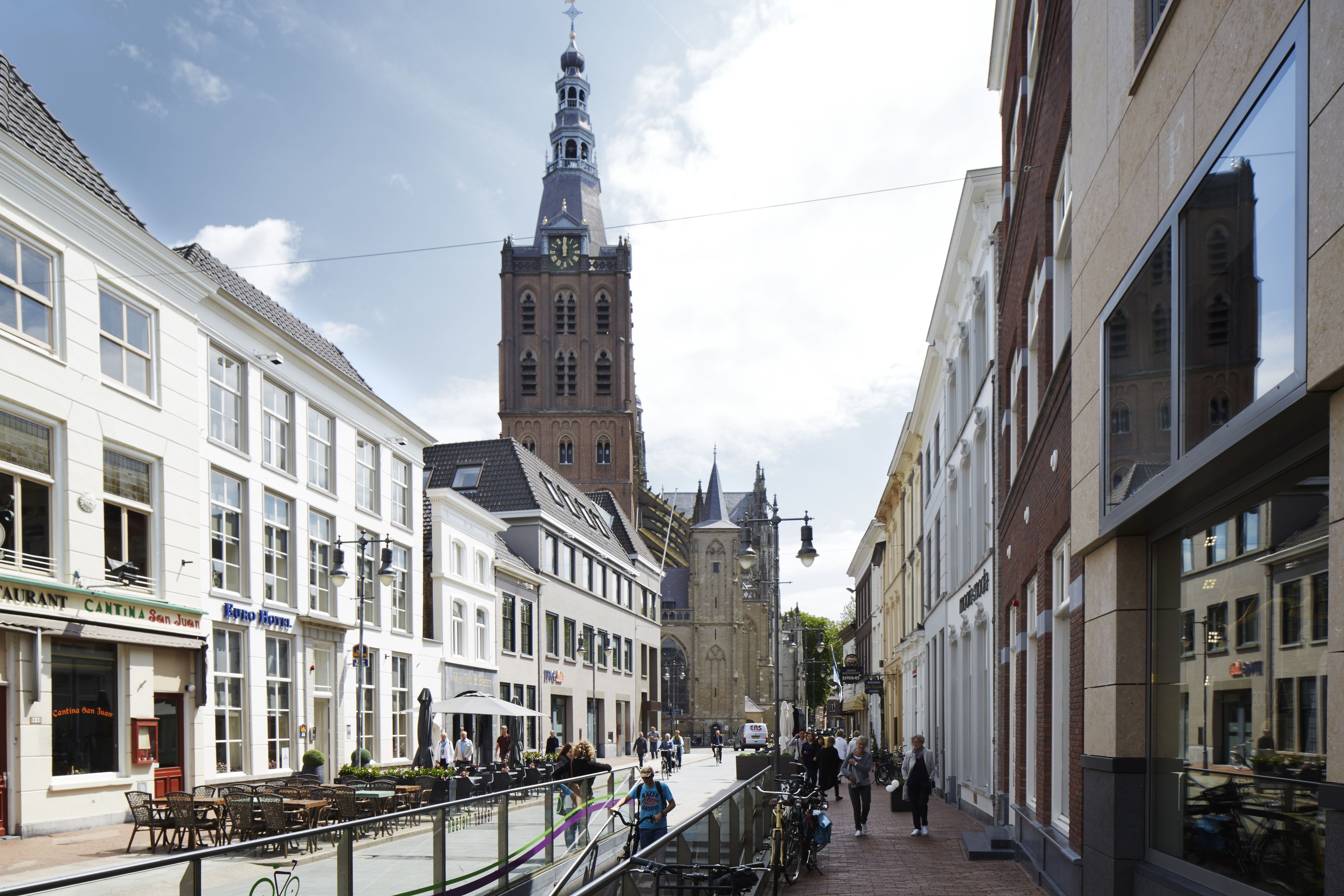 A street with buildings, a clock tower, and outdoor seating areas.