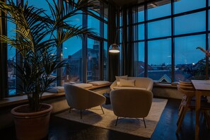 A modern living room with large windows, a potted plant, and a dining area. - The Duke Boutique Hotel ('s-Hertogenbosch)