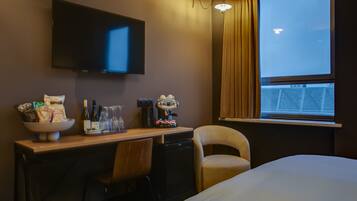 Een hotelkamer met een bed, een bureau met een schaaltje snacks, een koffiezetapparaat en een televisie aan de muur.