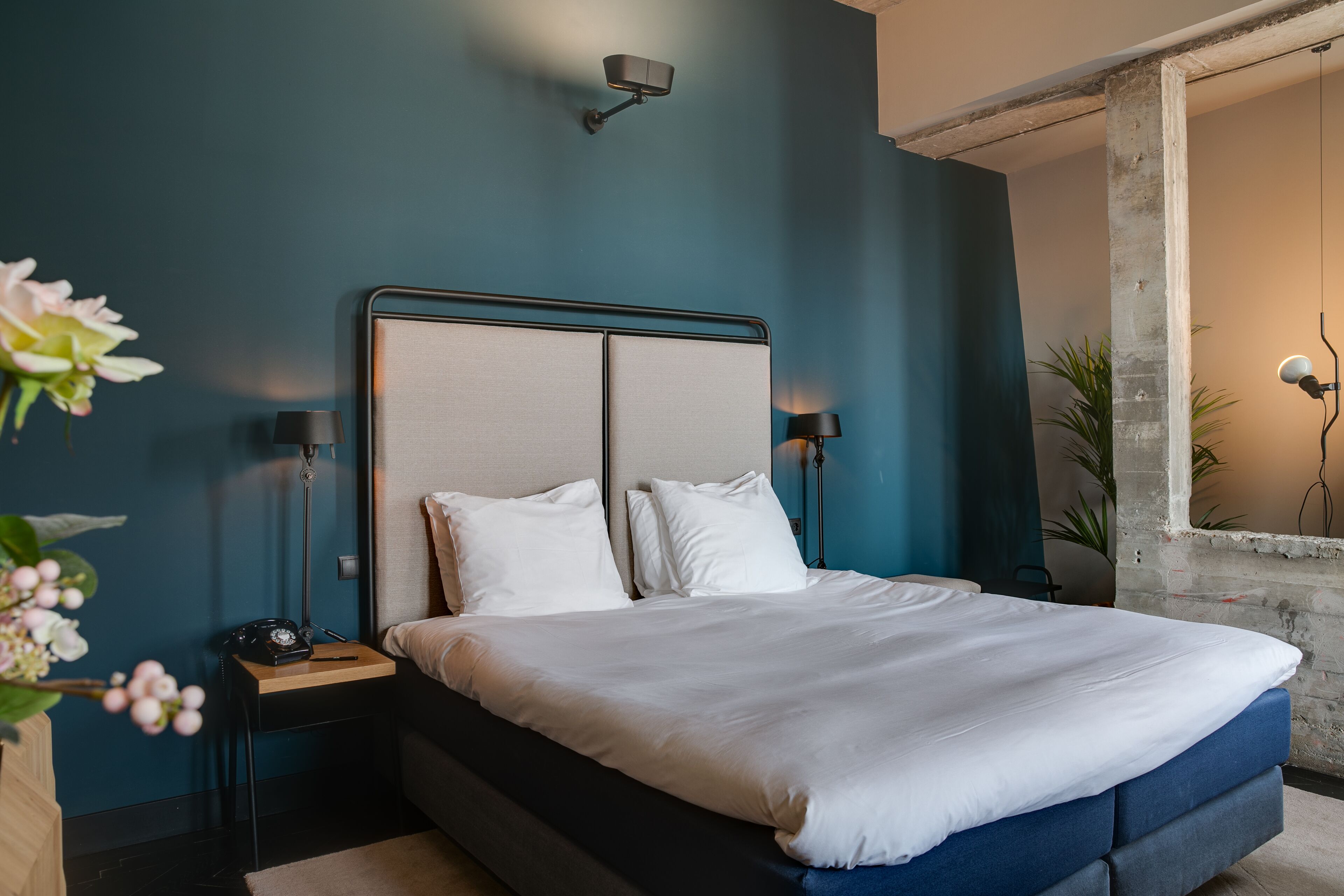Un dormitorio con una cama, lámparas de noche, una mesita de noche y un florero con flores.