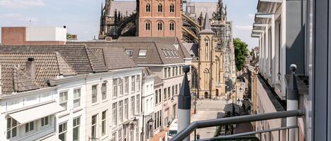 A balcony with a table and chairs overlooking a city street with historic buildings and a prominent tower.