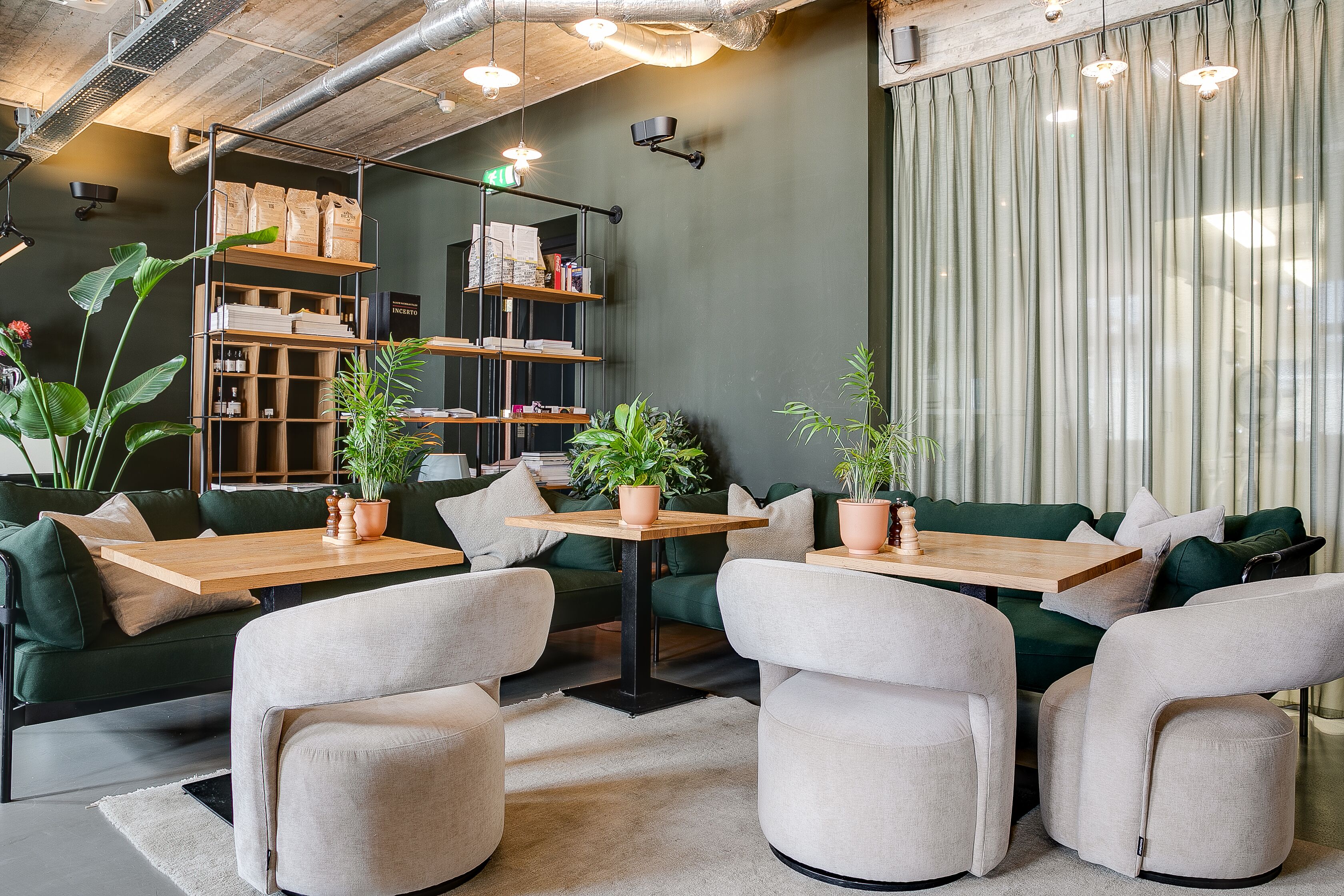 A modern interior with green sofas, wooden tables, and potted plants.