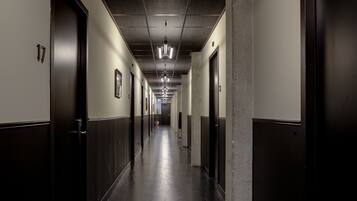 Een lange, smalle hotelgang met deuren aan beide kanten, genummerde bordjes en een centraal lichtarmatuur.