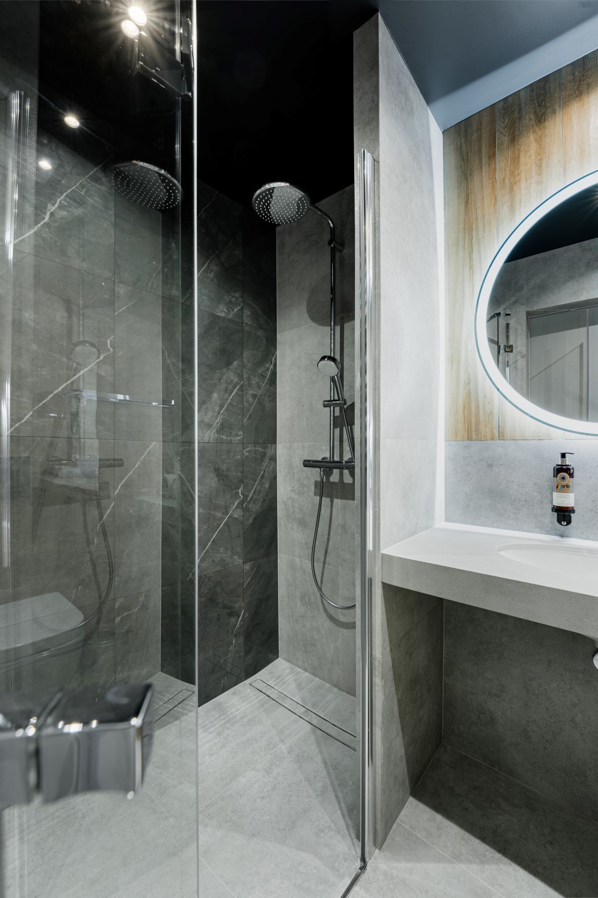 Un baño moderno con ducha de vidrio, piso de baldosas de mármol y tocador de madera con espejo redondo.