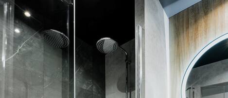 Un baño moderno con ducha de vidrio, piso de baldosas de mármol y tocador de madera con espejo redondo.