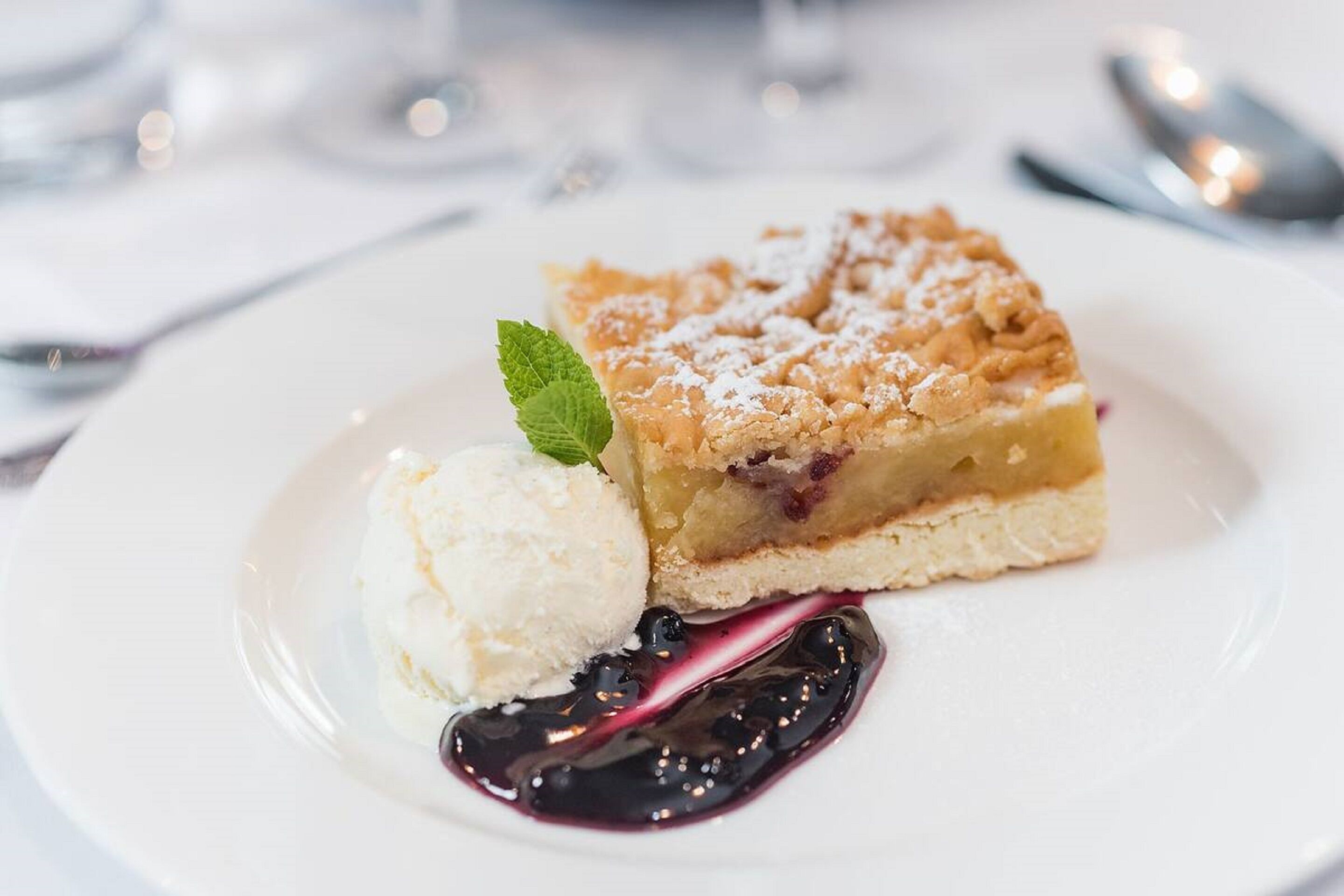 A dessert plate with a slice of pie, a scoop of ice cream, and a berry sauce.
