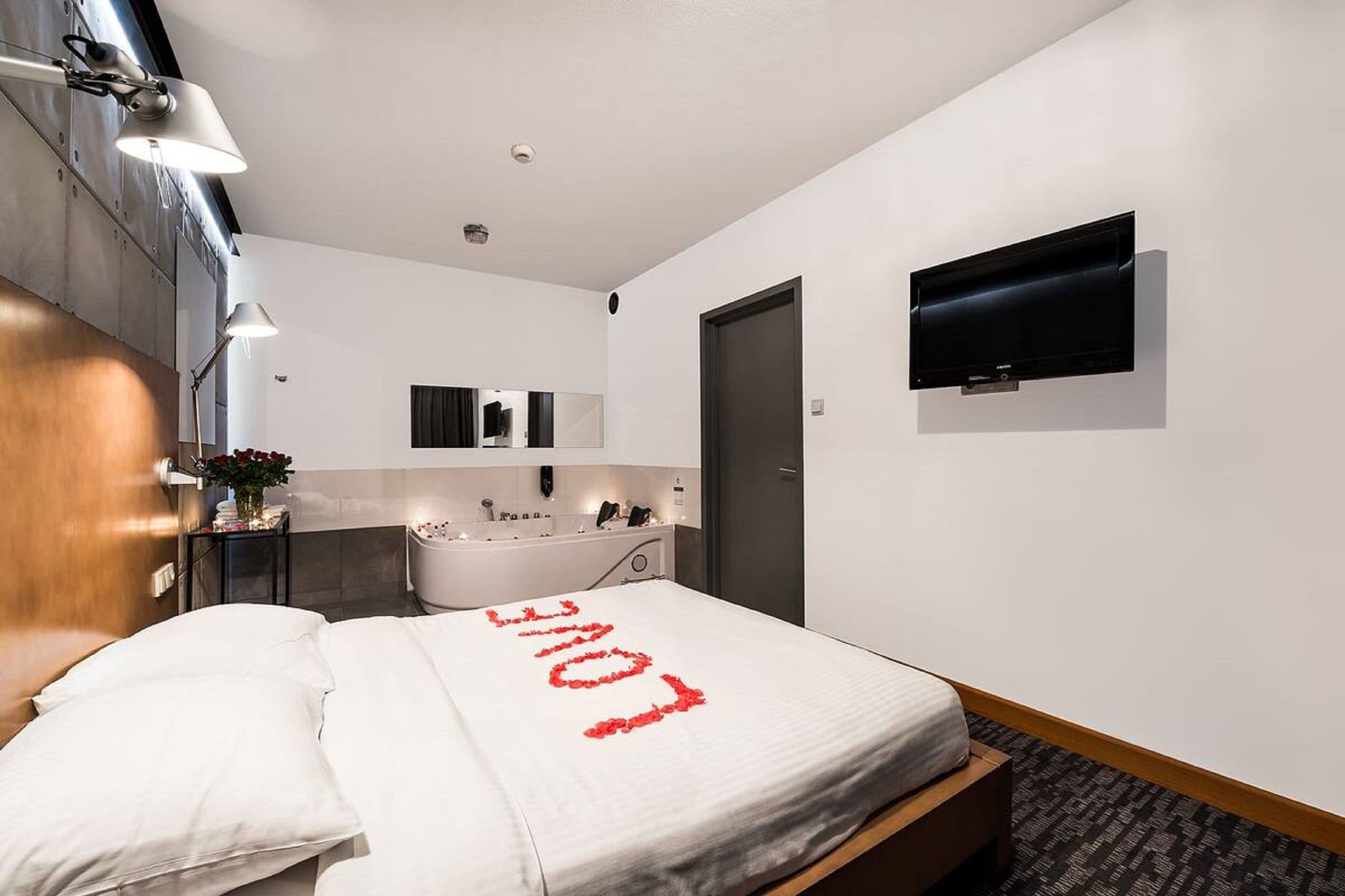 A hotel room with a bed, a TV, a bathroom with a bathtub, and a mirror.