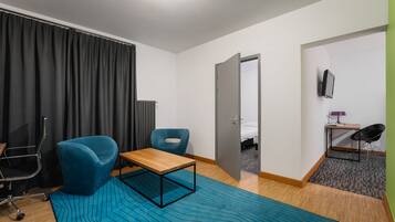 A hotel room with a bed, a desk, two chairs, a table, a radiator, a TV, and a window with curtains.