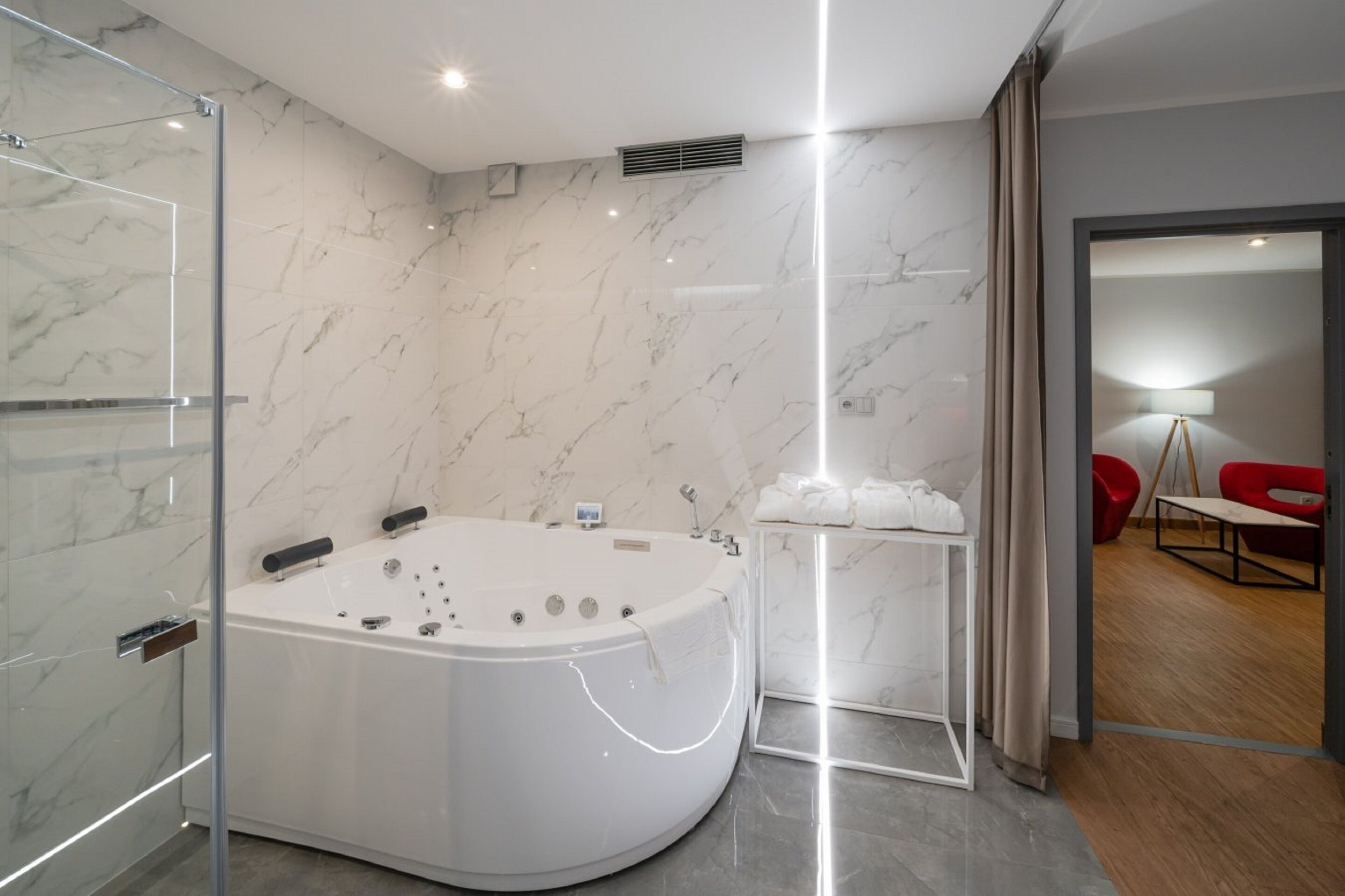 A modern bathroom with a freestanding bathtub, marble walls, and a glass shower enclosure.