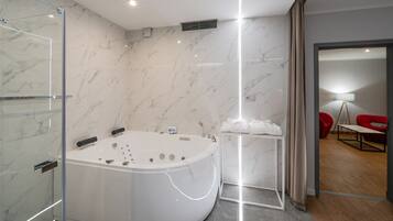A modern bathroom with a freestanding bathtub, marble walls, and a glass shower enclosure.
