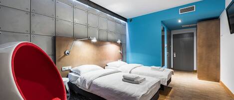 Una habitación de hotel moderna con una cama grande, una silla roja y una pared azul decorativa.