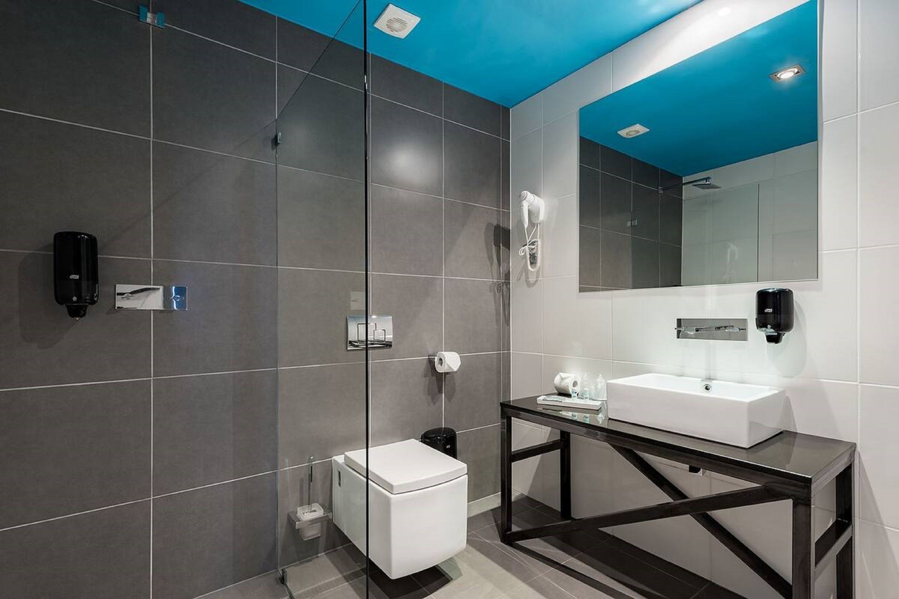 Un baño moderno con un lavamanos blanco, cabina de ducha de vidrio y techo azul.