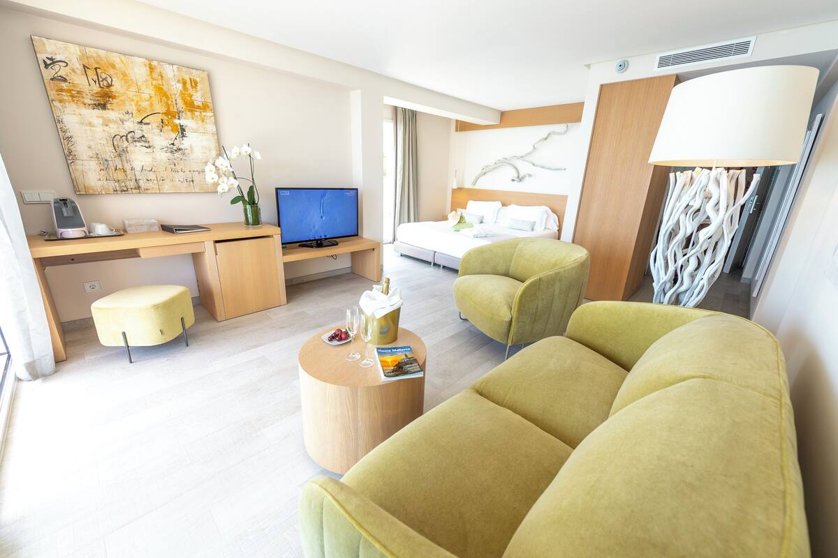 A modern hotel room with a bed, a desk with a computer, a TV, and a sofa.
