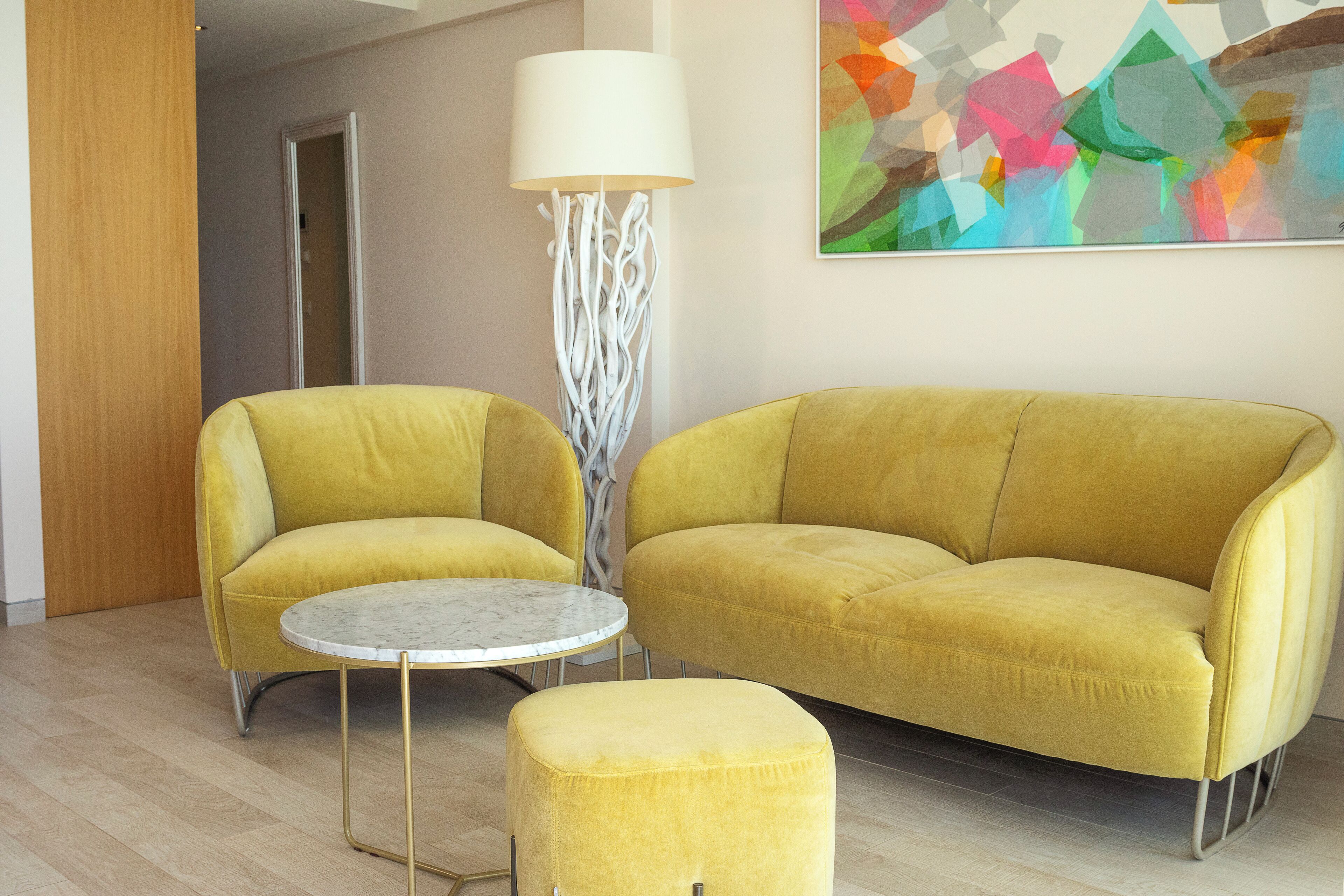 Un salon moderne avec un canapé jaune, un pouf assorti et une petite table ronde.