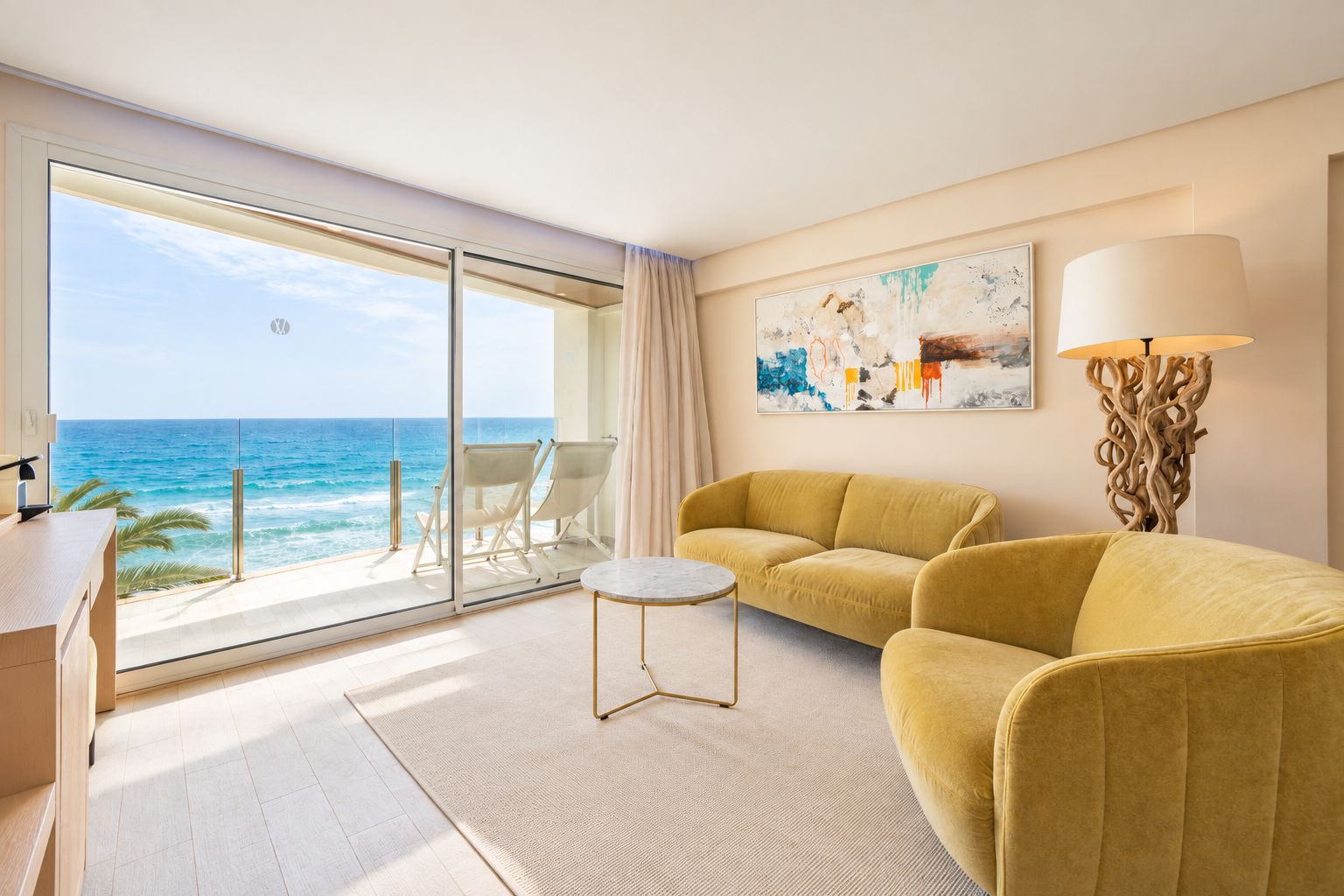 A room with a large window overlooking the ocean, a yellow sofa, a small round table, and a modern lamp.