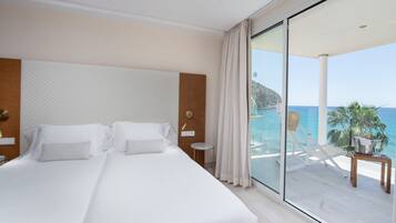 A hotel room with a large bed, a view of the sea, a balcony with a table and chairs, and a wooden headboard.