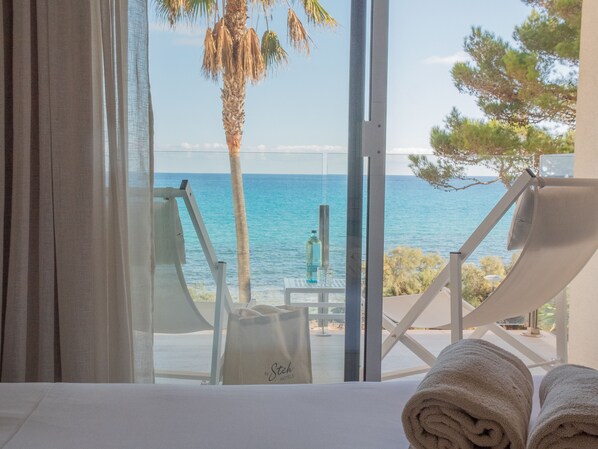 A room with a view of the sea, a beach chair, a towel, and a table with a bottle. - Melbeach Hotel & Spa - Adults Only (Capdepera)