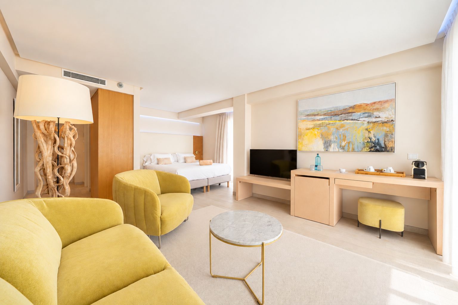 A hotel room with a bed, a desk, a TV, a sofa, and a painting on the wall.