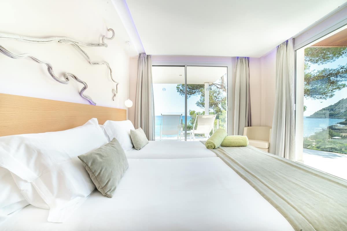 A hotel room with a large bed, a chair, and a view of the sea.