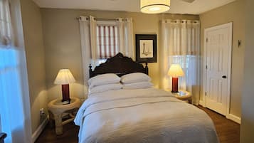 A bedroom with a large bed, two bedside lamps, a framed picture on the wall, and a door to the right.